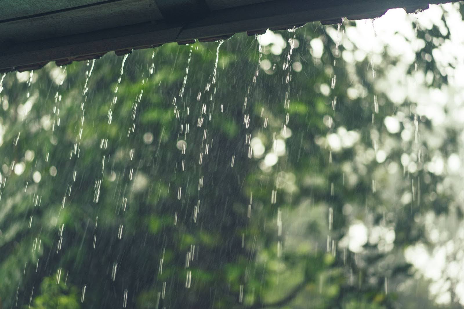 Heavy rain pouring from a roof edge during a storm, illustrating the risk of seasonal roof damage in California caused by extreme weather conditions.